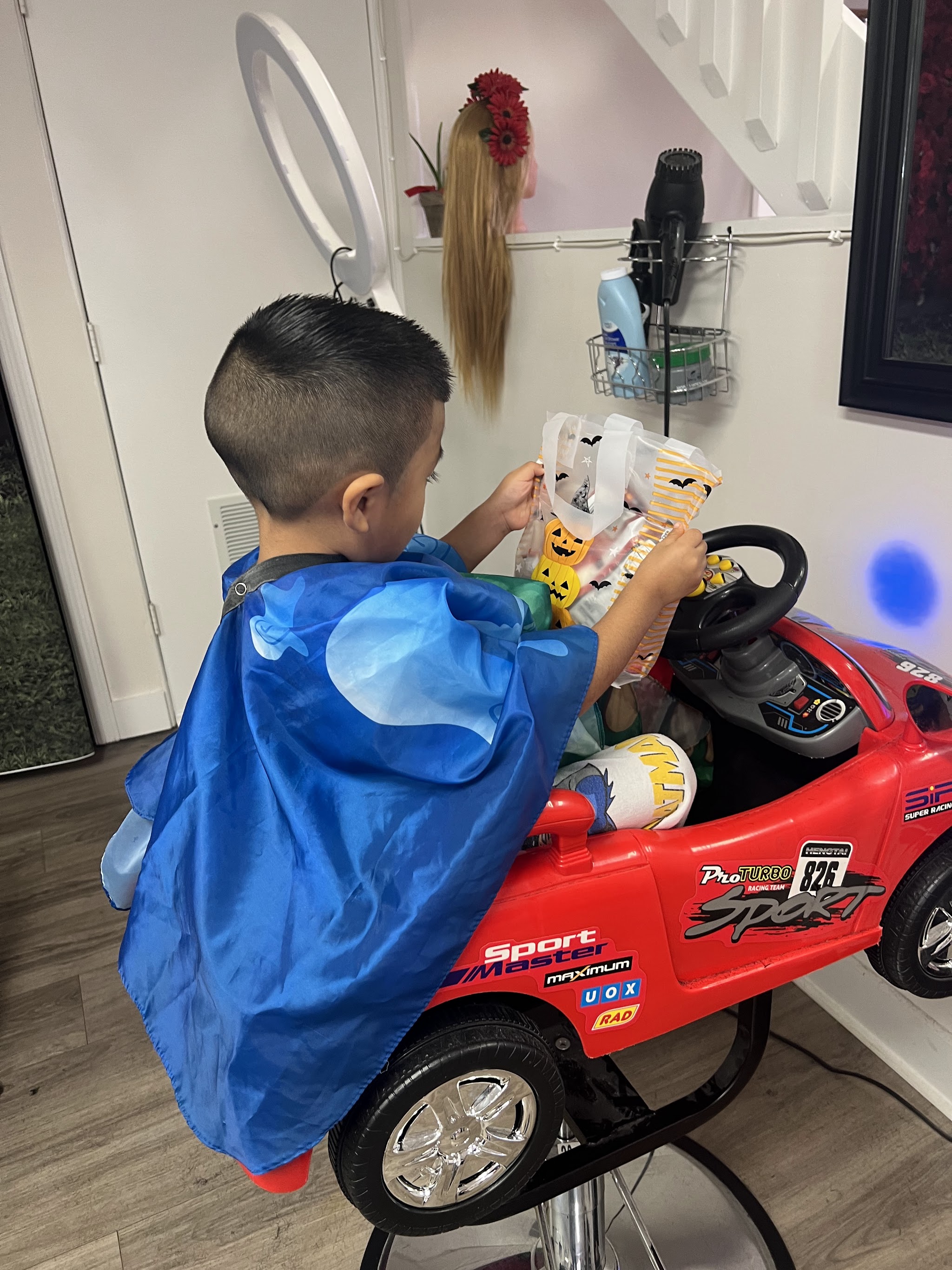 A little boy in our race-car chair holding a Halloween treat bag after his haircut
